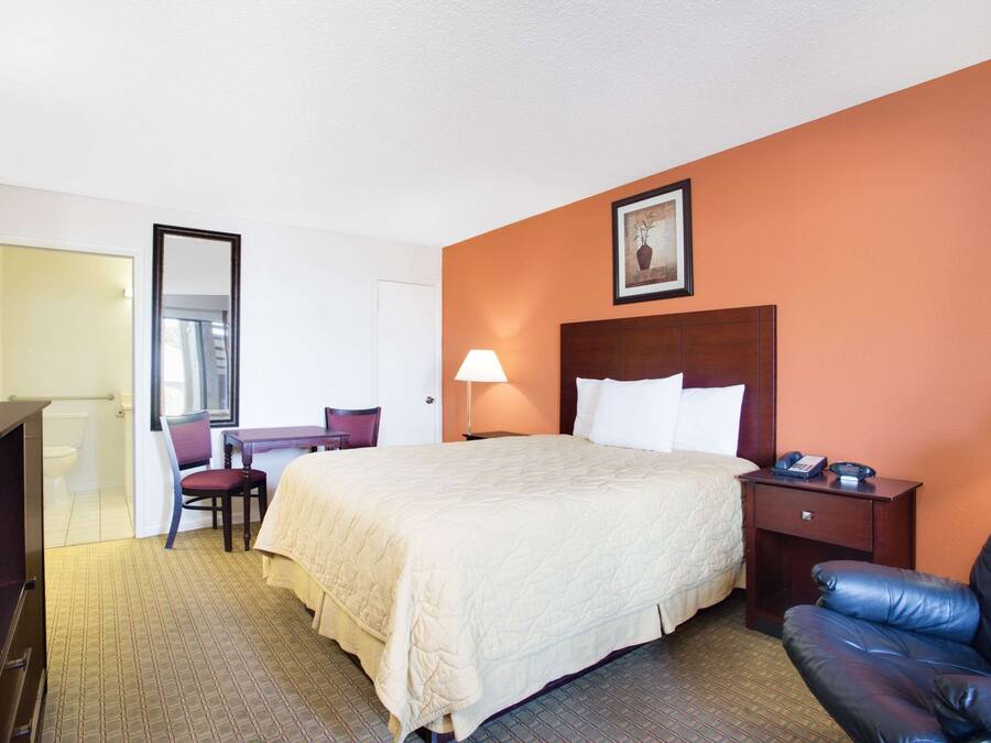 A hotel room with a bed, a desk, a chair, a nightstand, and a large mirror.