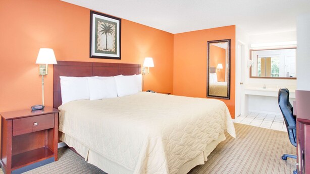 A hotel room with a bed, two bedside tables with lamps, a large mirror, and a framed picture on the wall. - Super 8 by Wyndham Defuniak Springs (De Funiak Springs)