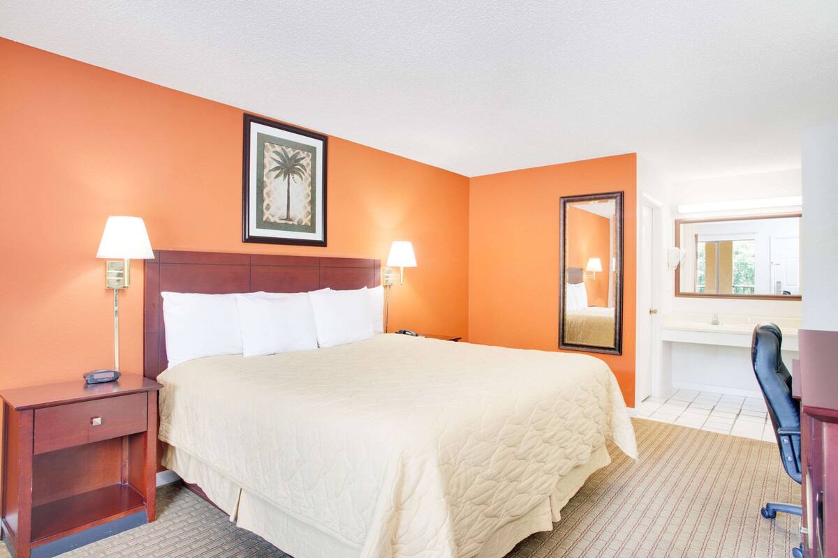 A hotel room with a bed, two bedside tables with lamps, a large mirror, and a framed picture on the wall.