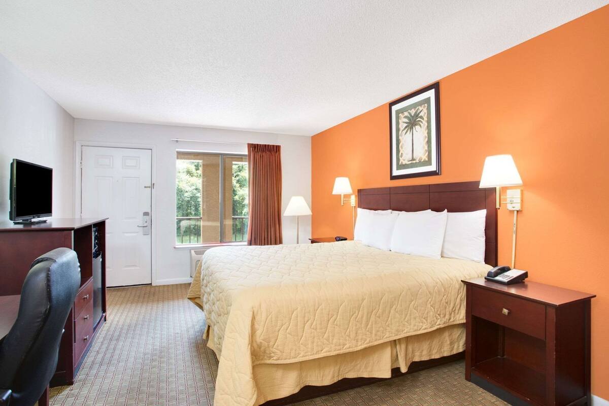 A hotel room with a bed, bedside lamps, a desk with a television, a chair, and a window with curtains.