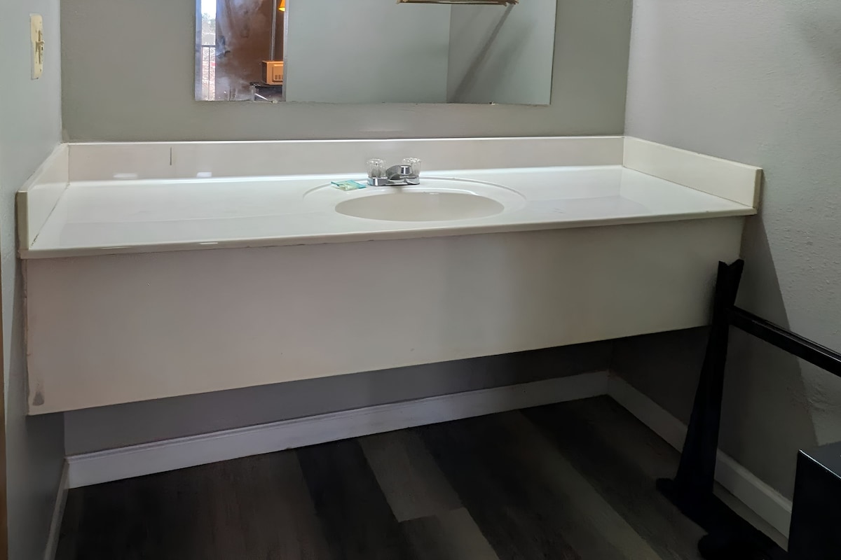 Ein Badezimmer mit weißem Waschbecken, Spiegel und dunklem Holzboden.