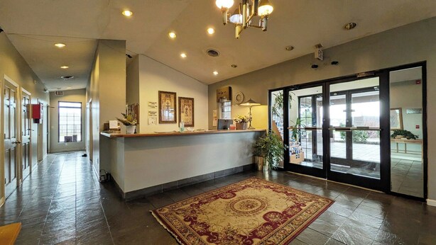 A hotel reception area with a reception desk, framed artwork, a clock, and a large glass door leading outside. - Inn of Loudon (Loudon)