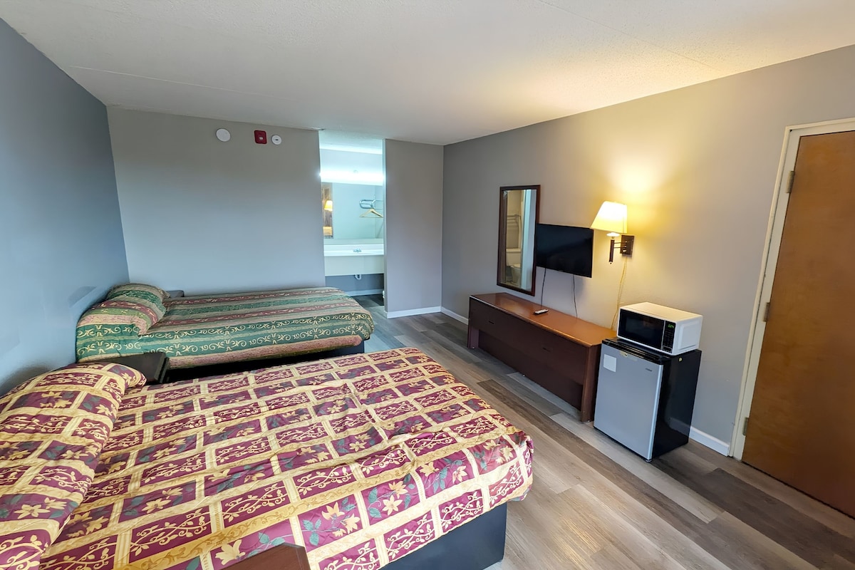Habitación de hotel con dos camas, un escritorio pequeño, televisor, microondas y una puerta.