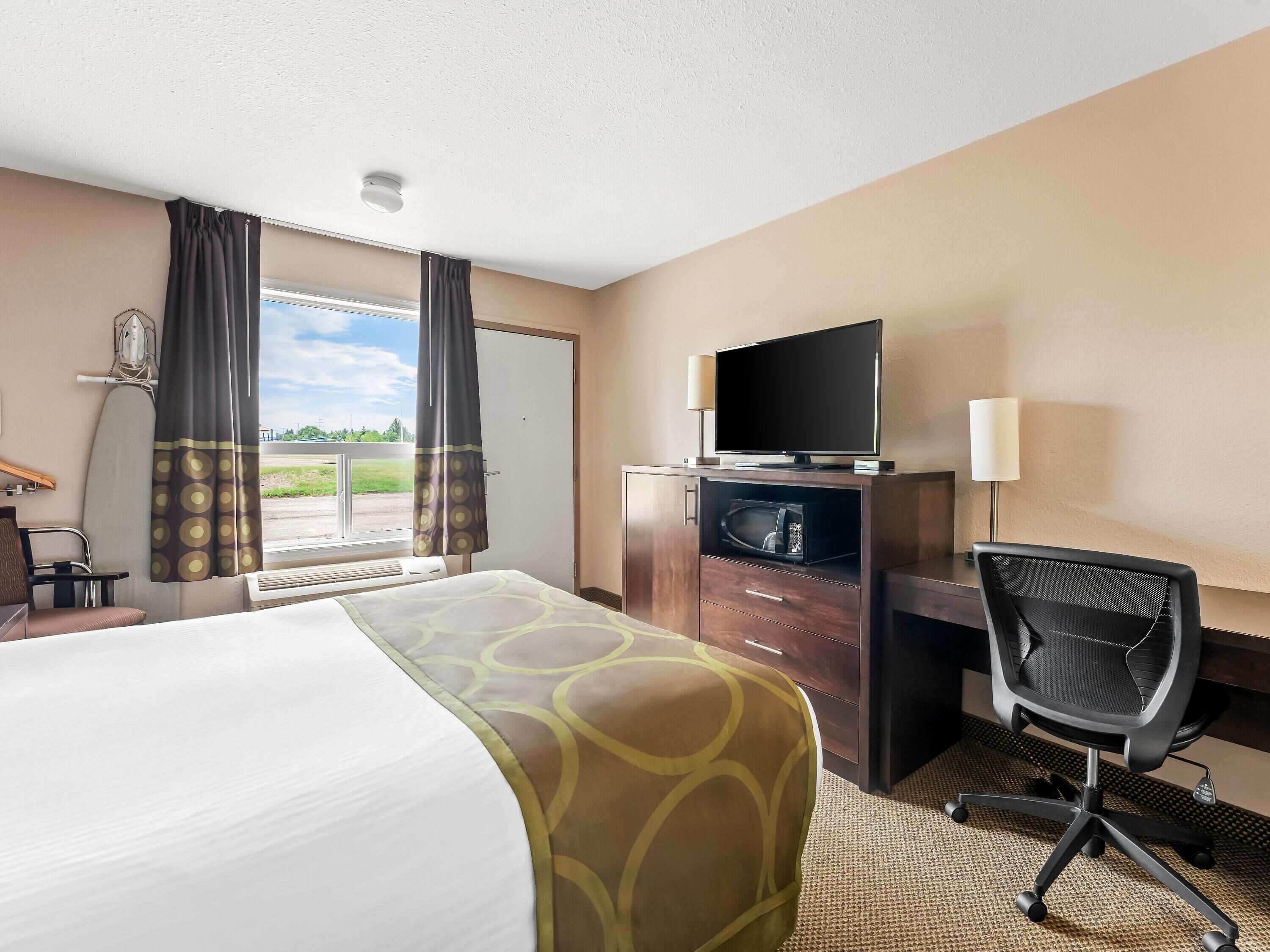 A hotel room with a bed, a desk with a TV, a chair, and a window with curtains.