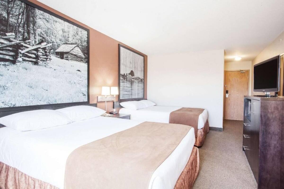 Hotellihuone, jossa on kaksi sänkyä, televisio, työpöytä ja suuri kehystetty taulu seinällä.