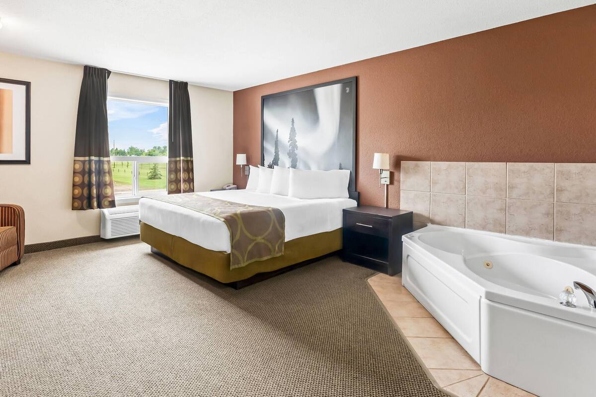 Hotellihuone, jossa on suuri sänky, erillinen kylpyhuone, ikkuna verhoilla ja näkymä ulos.