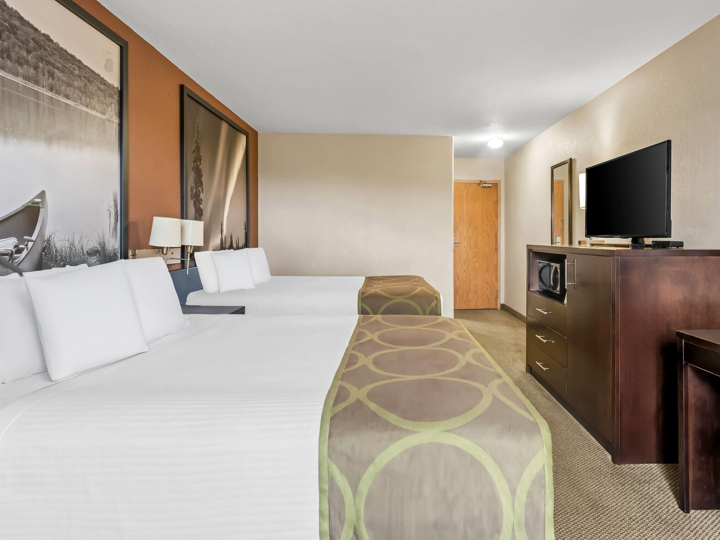 Habitación de hotel con dos camas, televisor, escritorio y puerta que da a otra habitación.