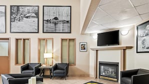 Eine Hotelhalle mit Kamin, Fernseher, gerahmten Bildern an den Wänden und einem Essbereich mit Stühlen und einem Tisch.