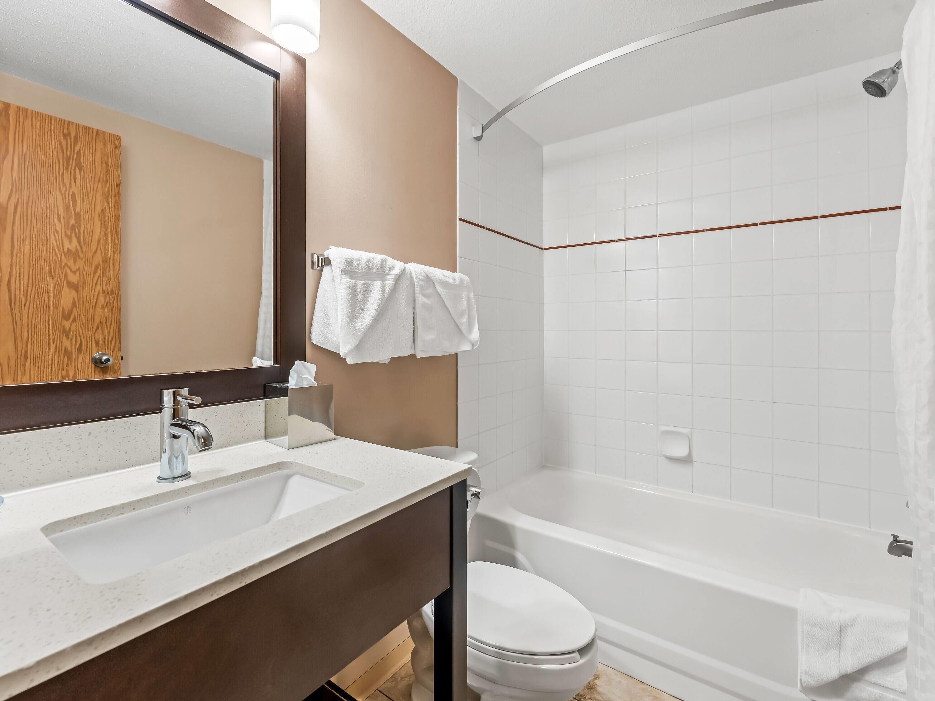 Une salle de bain moderne équipée d’un lavabo, d’un miroir, de toilettes et d’une baignoire.