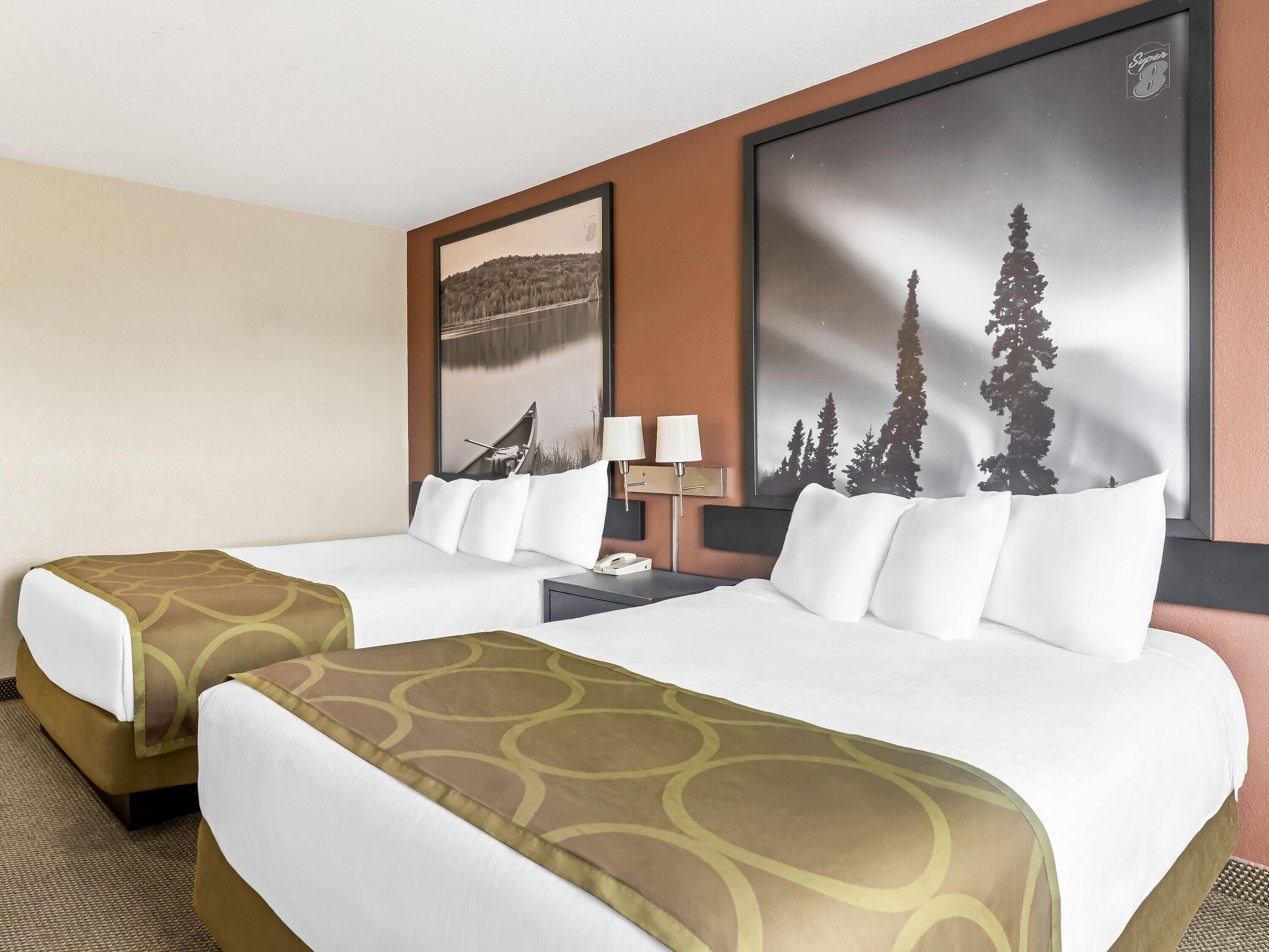 A hotel room with two beds, a nightstand, a lamp, and two large framed pictures on the wall.