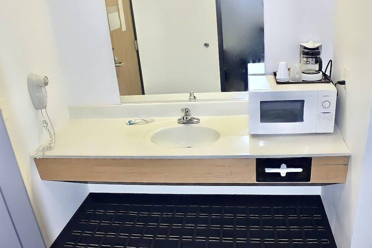 A bathroom with a sink, a mirror, a microwave, and a coffee maker.