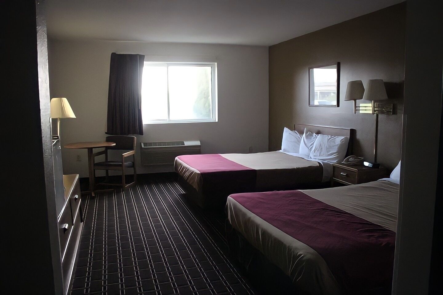 A hotel room with two beds, a desk, a chair, a window, and a nightstand with lamps.