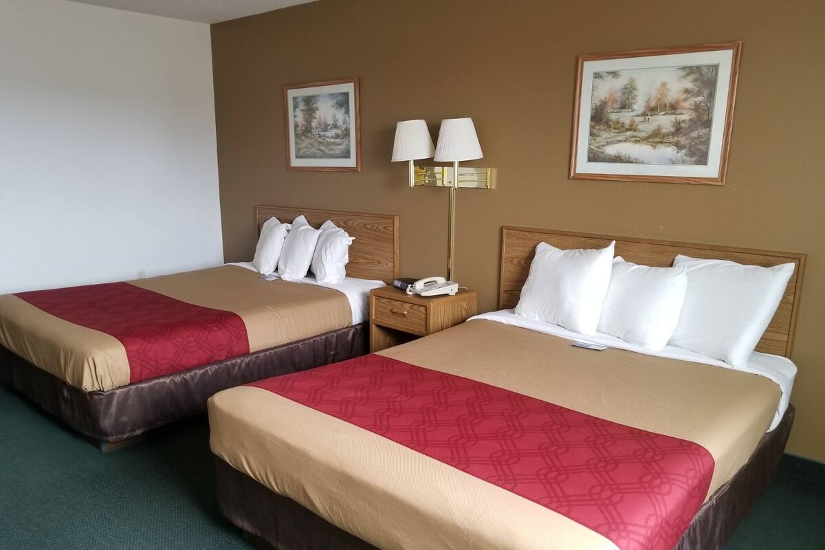 A hotel room with two beds, each with a wooden headboard, a nightstand with a lamp, and two framed pictures on the wall.