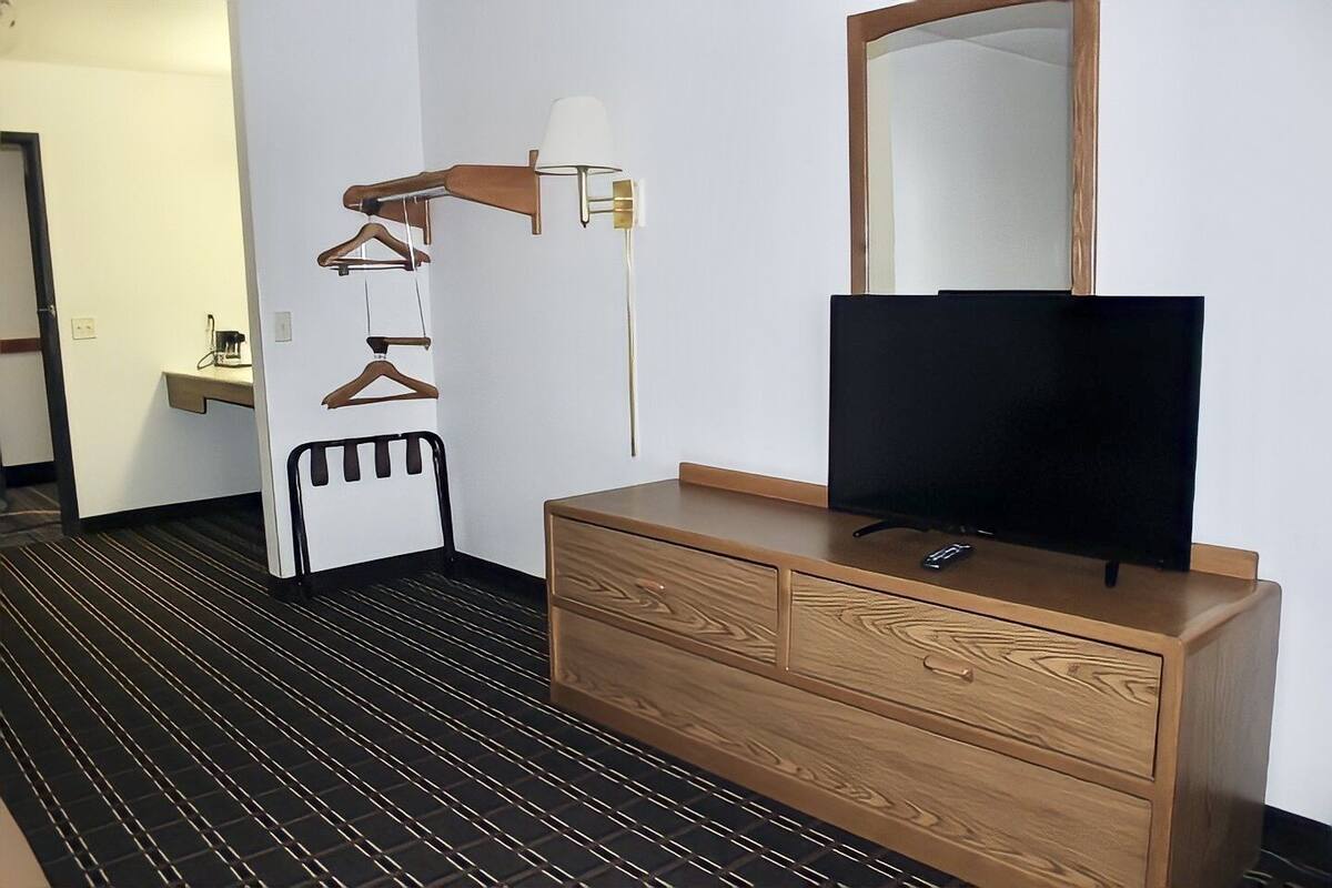 A hotel room with a wooden dresser, a flat-screen TV, a mirror, and a coat rack with hangers.