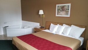A hotel room with a large bed, a separate bathtub, a bedside table with a lamp, and a framed picture on the wall. - AmeriVu Inn and Suites - Stanley (Stanley)