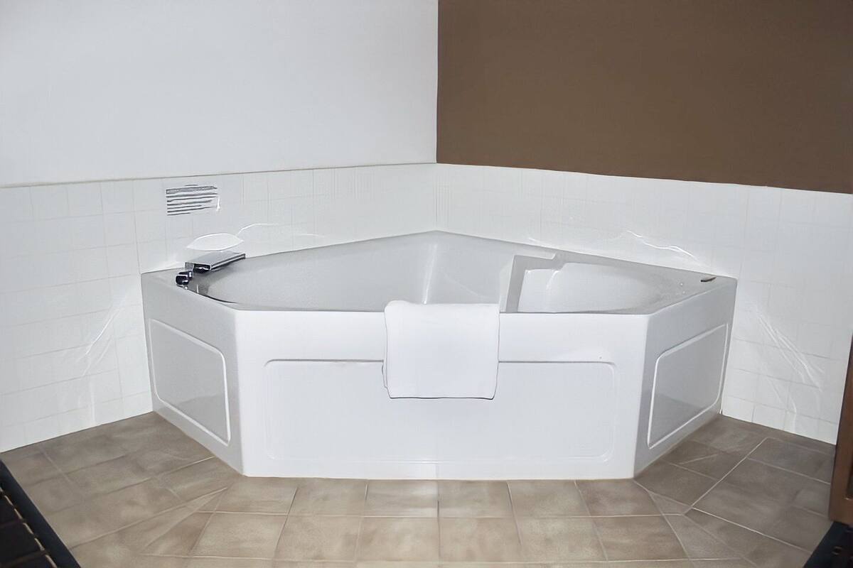 A corner bathtub with a towel, white tiled walls, and a brown accent wall.