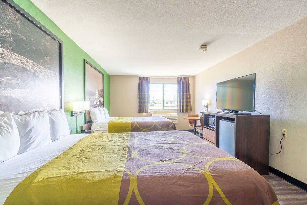 Habitación de hotel con dos camas, televisión, escritorio con silla y ventana con cortinas.