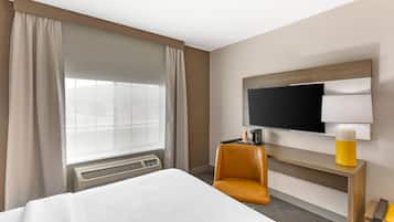 Une chambre d’hôtel avec un lit, une télévision, une chaise et une petite table avec une lampe.