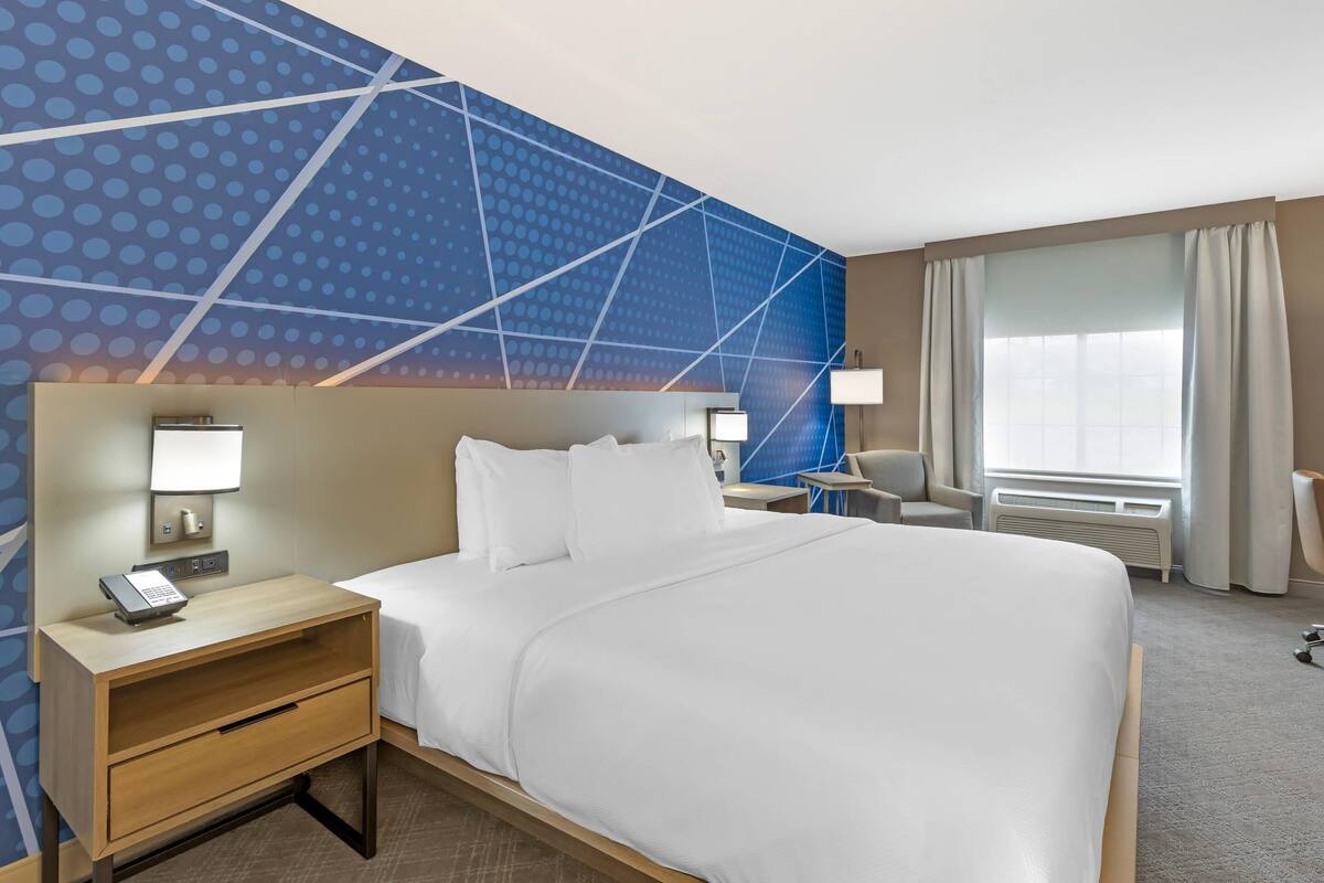 Une chambre d’hôtel avec un grand lit, des tables de chevet avec des lampes, un bureau et une fenêtre avec des rideaux.