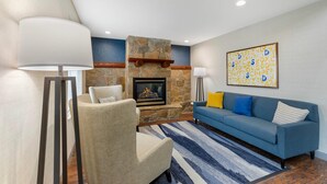 A living room with a stone fireplace, a blue sofa, and a lamp. - Comfort Inn & Suites Summerset - North Rapid City (Blackhawk)