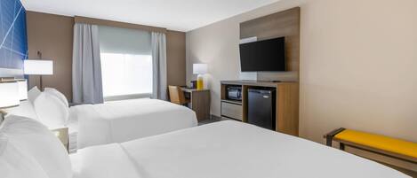 A hotel room with two beds, a desk, a television, and a bench.