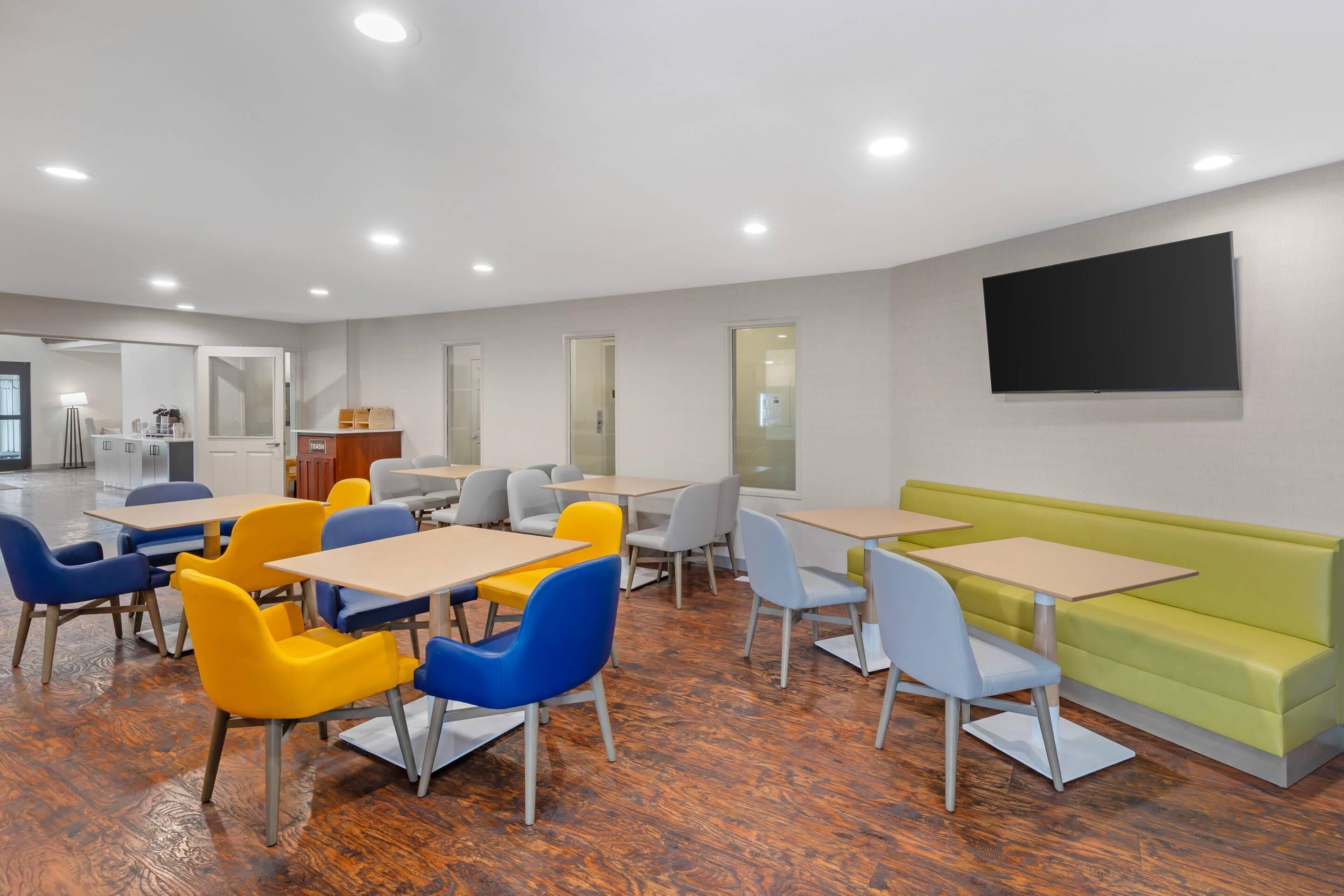 A modern dining area with tables and chairs, a green sofa, and a flat-screen TV mounted on the wall.