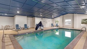 An indoor swimming pool with a tiled edge, a covered area with chairs, and a view of the outside. - Comfort Inn & Suites Summerset - North Rapid City (Blackhawk)