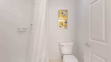 A bathroom with a toilet, a shower curtain, and a framed artwork on the wall.