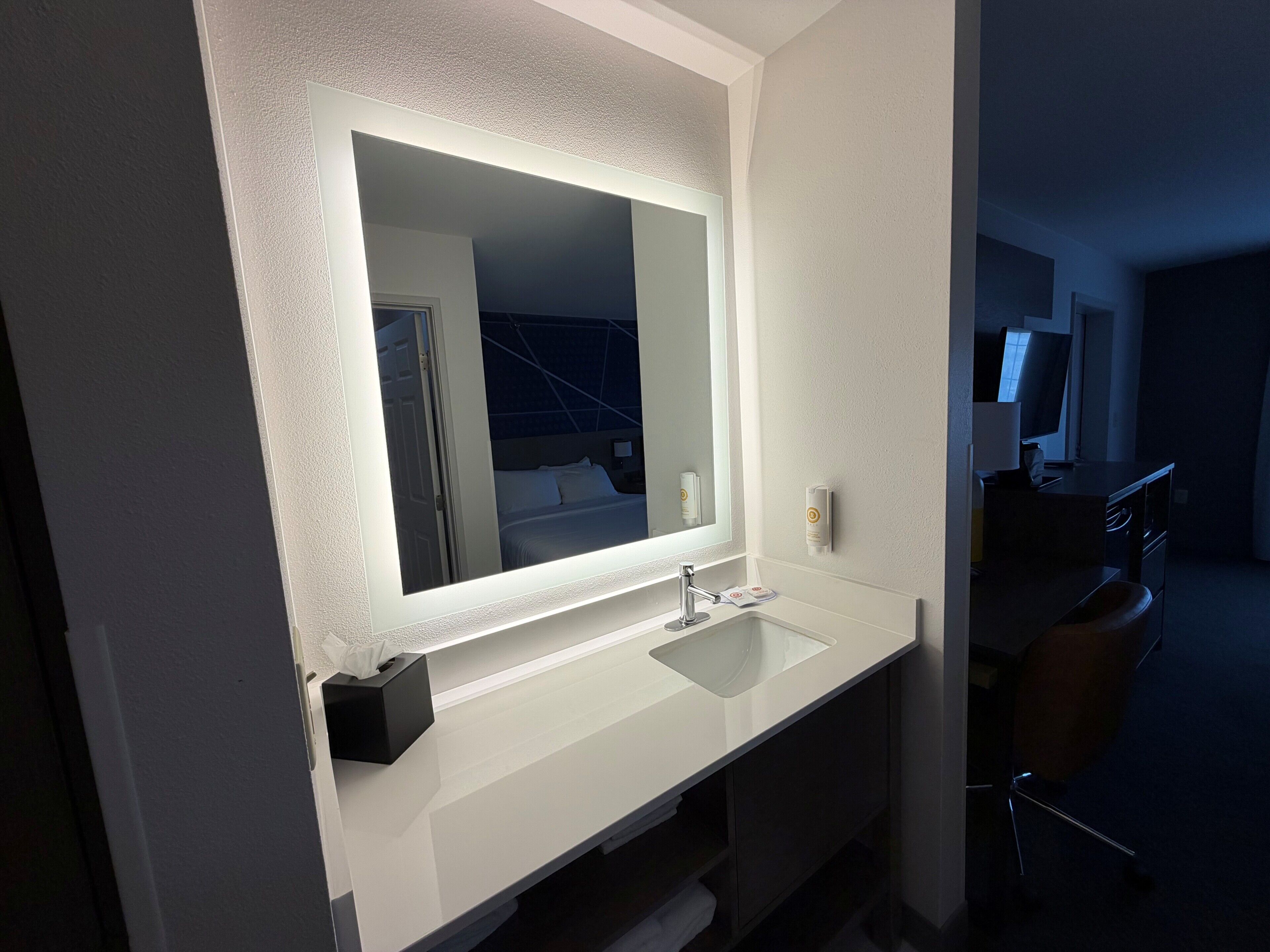 Un baño moderno con un espejo grande, lavabo blanco y un perchero para toallas.