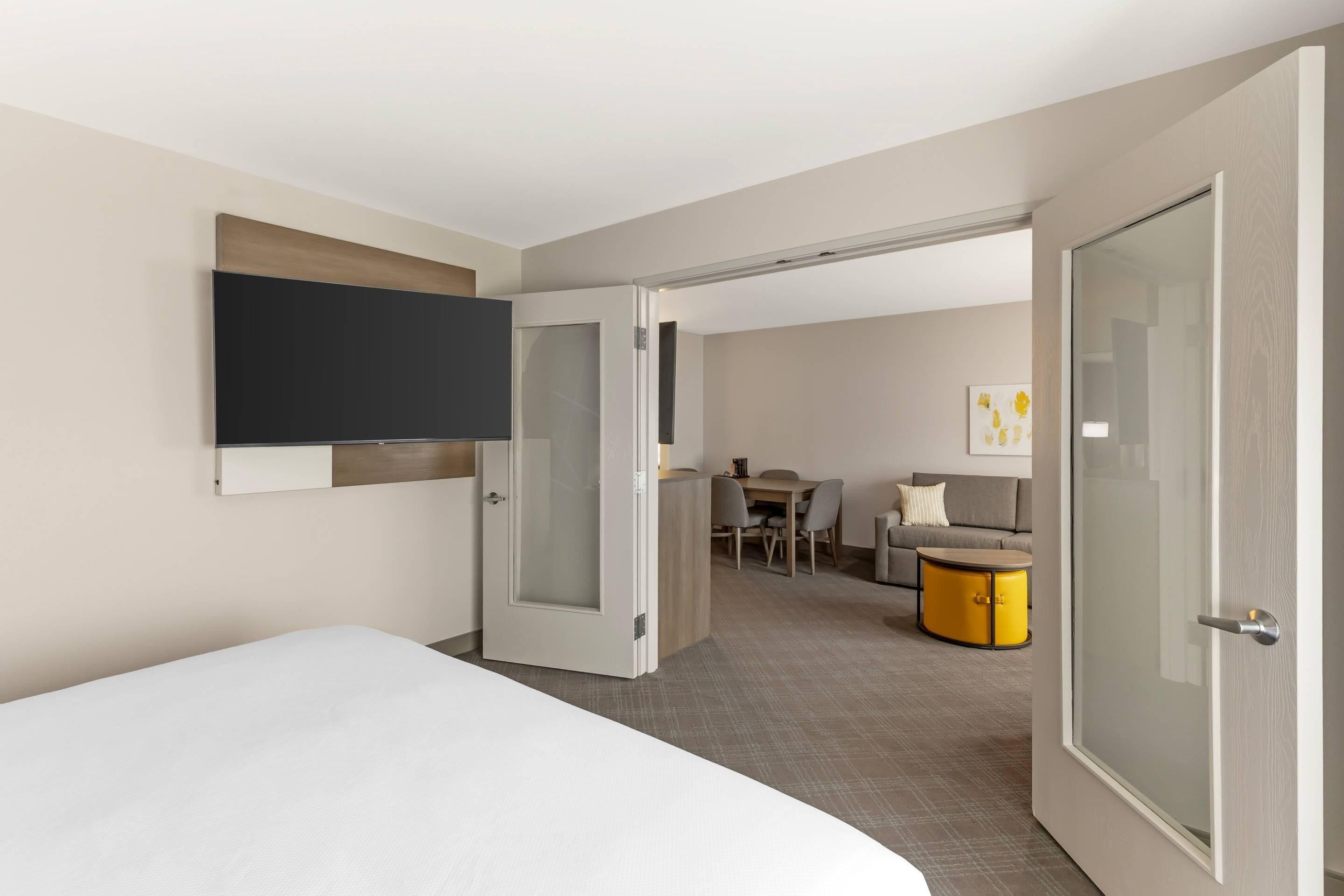 Ein Hotelzimmer mit Bett, Wandfernseher, Schreibtisch mit Stühlen und einer Couch.