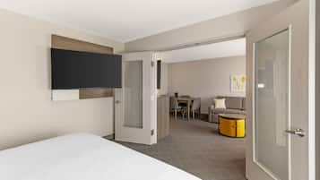 Ein Hotelzimmer mit Bett, Wandfernseher, Schreibtisch mit Stühlen und einer Couch.