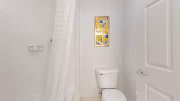 A bathroom with a toilet, a shower curtain, and a framed artwork on the wall.