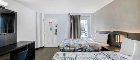 A hotel room with two beds, a desk, and a TV.