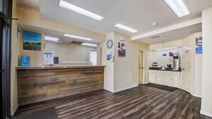 Un espace d’accueil comprenant un comptoir de réception en bois, une horloge et un réfrigérateur.