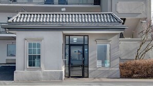 Un bâtiment avec un toit recouvert de tuiles, une porte d’entrée en verre et une petite fenêtre sur le côté.