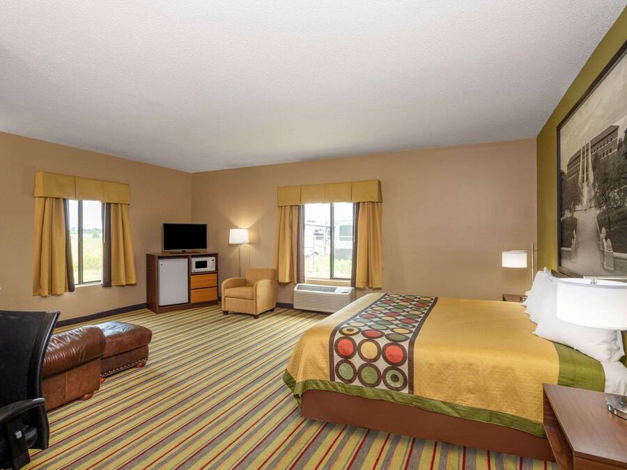 A hotel room with a bed, a desk, a chair, an ottoman, a television, and a painting on the wall.