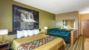Habitación de hotel con cama, un cuadro grande de una cascada, baño con bañera y alfombra a rayas.