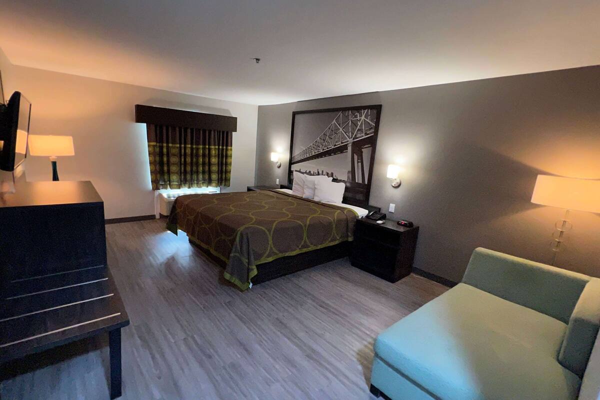Una habitación de hotel con cama, escritorio, silla y un ventanal con cortinas.