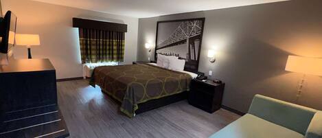 A hotel room with a bed, a desk, a chair, and a large window with curtains.