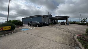 Un estacionamiento con entrada a un edificio, un letrero que indica la entrada y un espacio de estacionamiento para discapacitados de color azul.