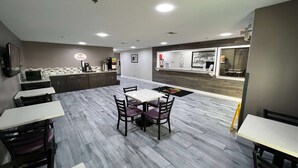 Un restaurante con un área de comedor central que presenta una mesa blanca y cuatro sillas, rodeado de armarios de madera y una cocina con una cafetera.