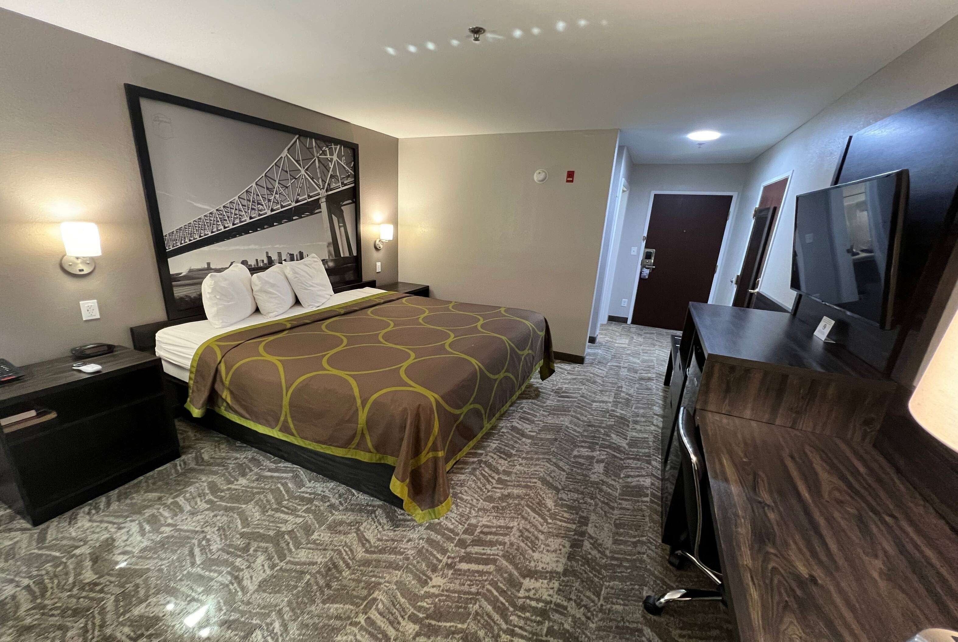 A hotel room with a bed, nightstands, a dresser, a television, and a large framed picture of a bridge.