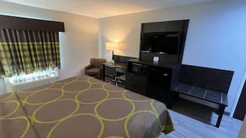A hotel room with a large bed, a desk with a chair, a television, and a bench.