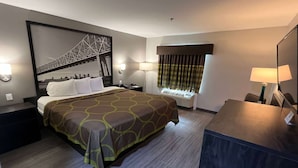 Habitación de hotel con una cama grande, un escritorio, una silla, una ventana con cortinas y un cuadro colgado en la pared que muestra un puente.