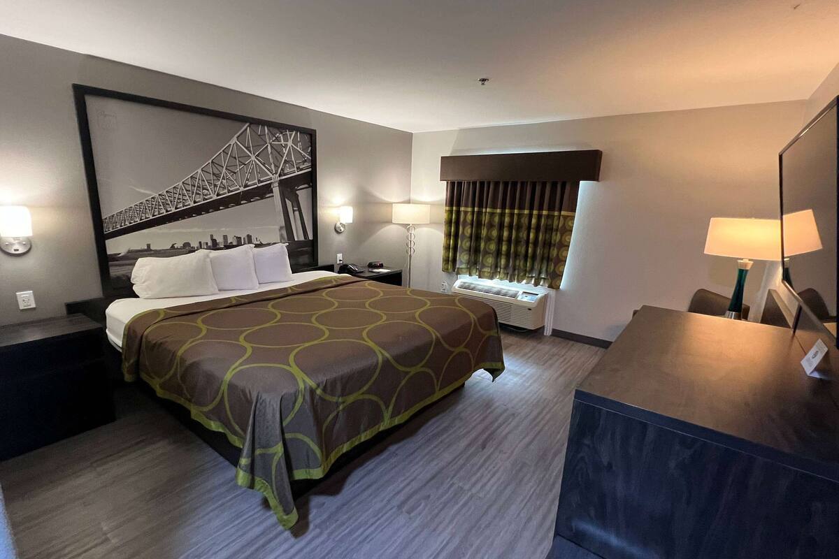 Habitación de hotel con una cama grande, un escritorio, una silla, una ventana con cortinas y un cuadro colgado en la pared que muestra un puente.