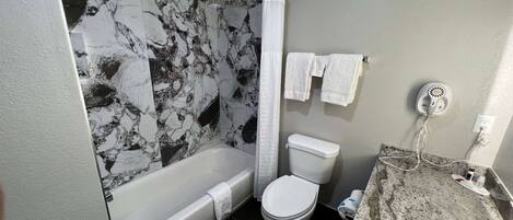 A bathroom with a bathtub, toilet, and a marble-patterned shower curtain.