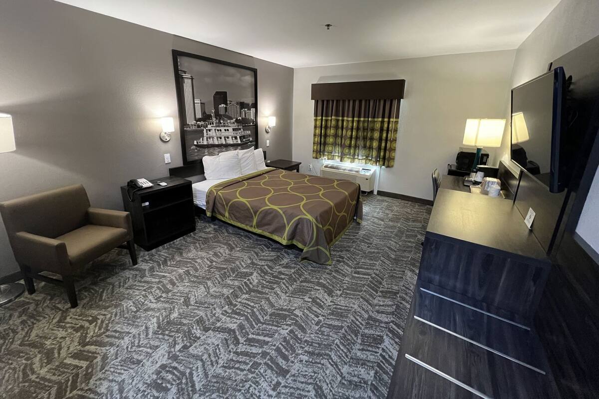 Habitación de hotel con cama, escritorio, silla, televisor y ventana con cortinas.