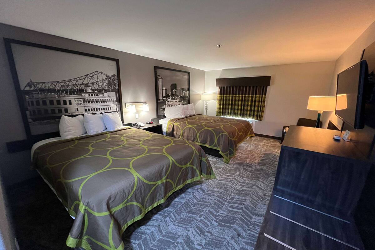 Habitación de hotel con dos camas, un cuadro grande con una vista urbana enmarcada, un escritorio con una lámpara y un televisor.