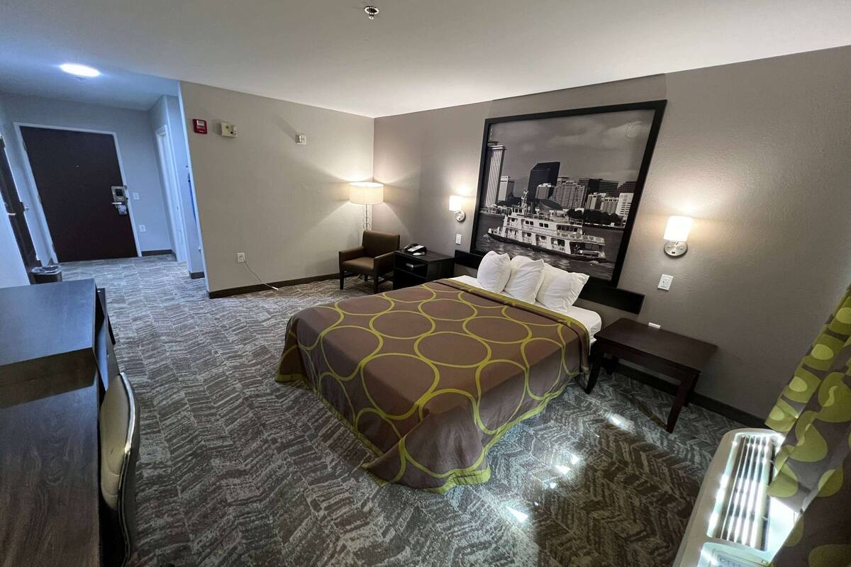 Una habitación de hotel con cama, escritorio, silla, mesita de noche y lámpara de pared.