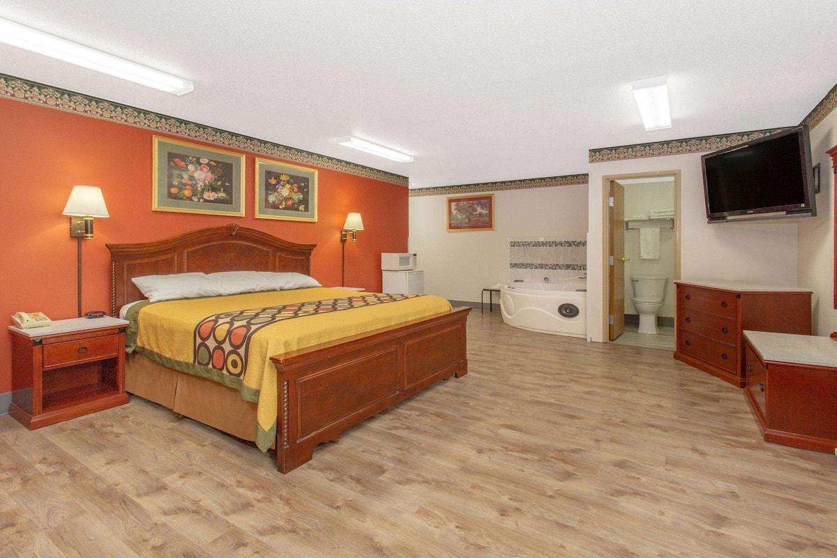 Hotelkamer met een houten bed, nachtkastje, bureau, stoel, televisie, badkamer met bad en toilet.